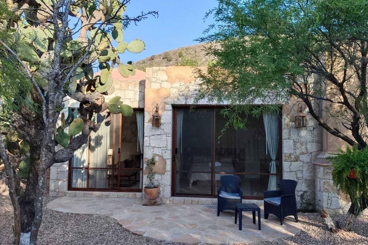 A stone building with large windows and a patio area with two chairs and a table.