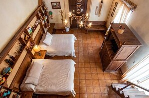 A narrow room with two beds, a wooden bench, a chandelier, and a wooden cabinet. - Hotel Centenario Los Arroyitos (Ezequiel Montes)