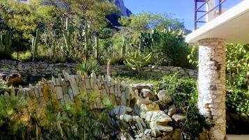 Un giardino con un muro in pietra, piante di cactus e una montagna sullo sfondo.