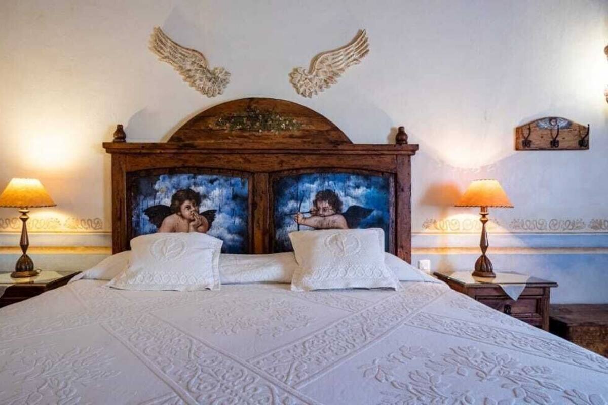 A bedroom with a large bed, two nightstands, and a wooden headboard with angel paintings.