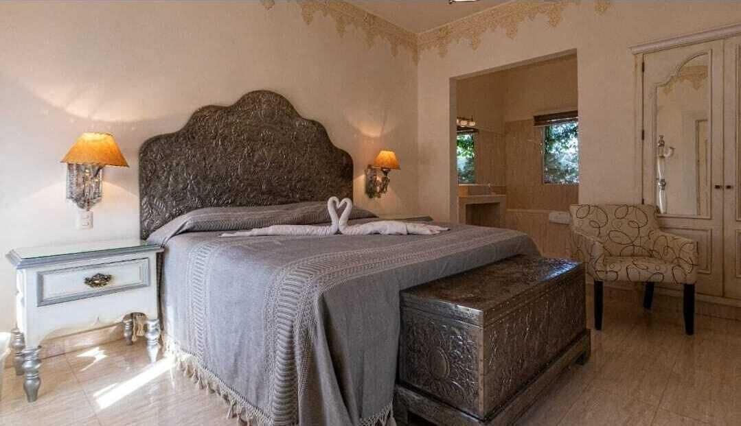 A bedroom with a large bed, two bedside lamps, a chest of drawers, a chair, and a wardrobe.
