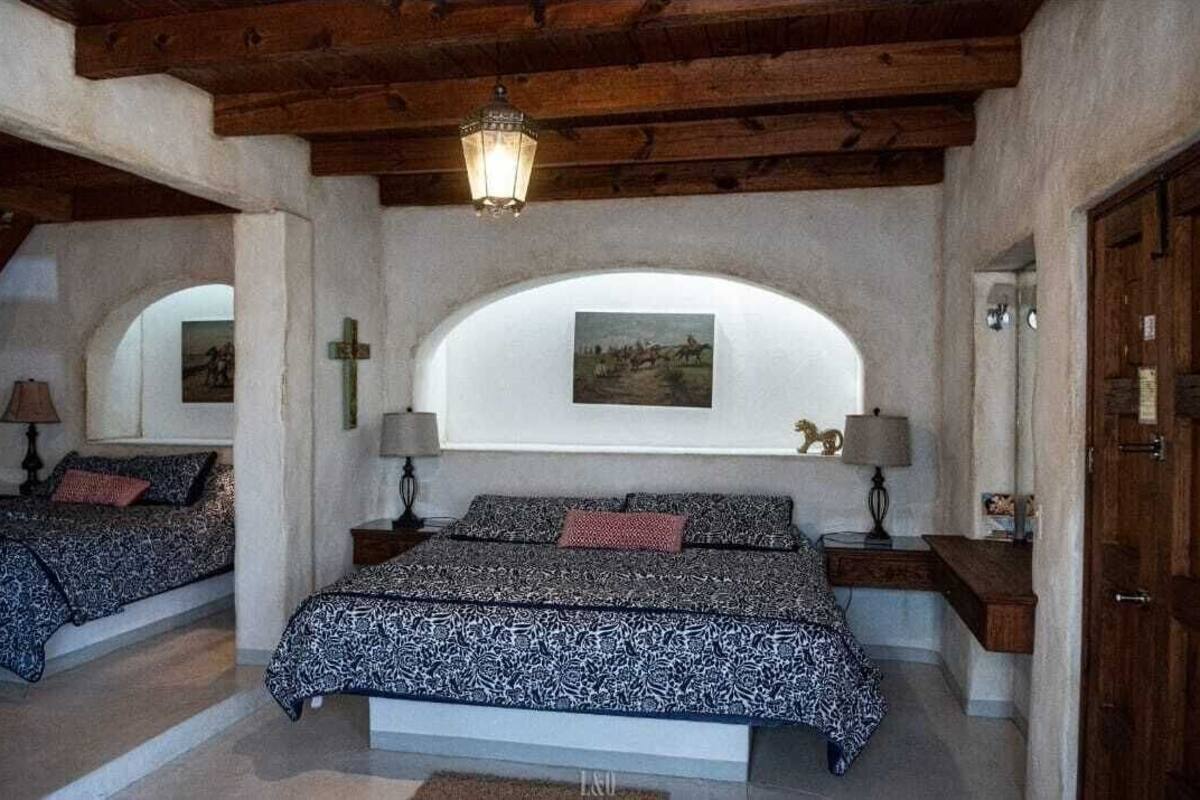 A bedroom with two beds, wooden beams, a cross on the wall, and a painting above the beds.