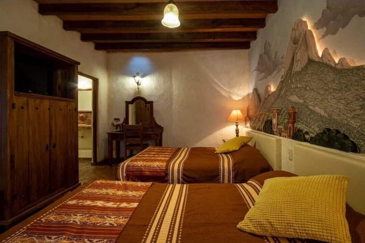 A room with two beds, wooden furniture, a wall-mounted lamp, and a mountain mural.