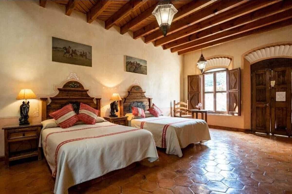 A traditional room with two beds, wooden beams, and a tiled floor.