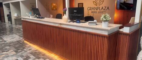 A hotel reception desk with a wooden finish, a clock, and a digital screen.