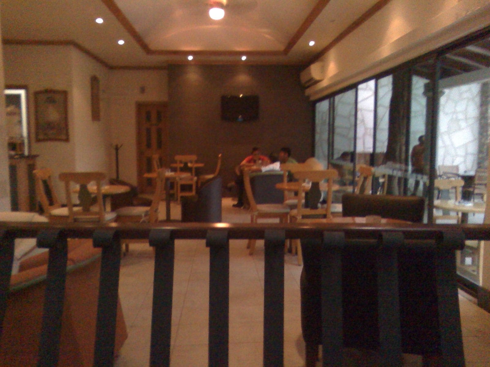 An indoor dining area with tables and chairs, a television screen, and large windows.