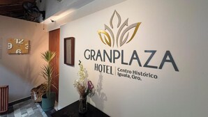 A hotel reception area with a clock, a logo for GranPlaza Hotel, and a vase with flowers. - Gran Plaza Hotel Centro Historico (Iguala de la Independencia)