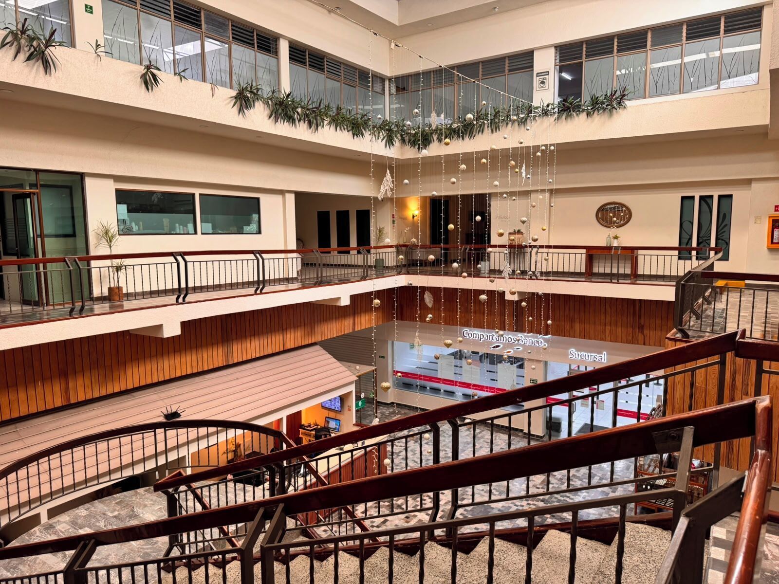 A multi-level atrium with a central open area, wooden railings, and potted plants.