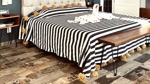 A modern bedroom with a tufted headboard, a striped bedspread, and a ceiling fan.