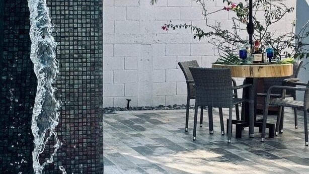 A pool area with a tiled wall, a table with chairs, and an umbrella.