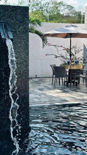 Un espace piscine agrémenté d’un mur carrelé, d’une table avec des chaises et d’un parasol.
