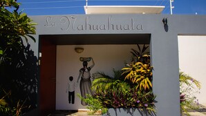 The entrance of La Nahuhuala with a mural of a woman holding a child, surrounded by tropical plants.