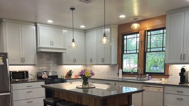 Una cocina moderna con armarios blancos, una isla central con taburetes y suelo de madera, con iluminación colgante.