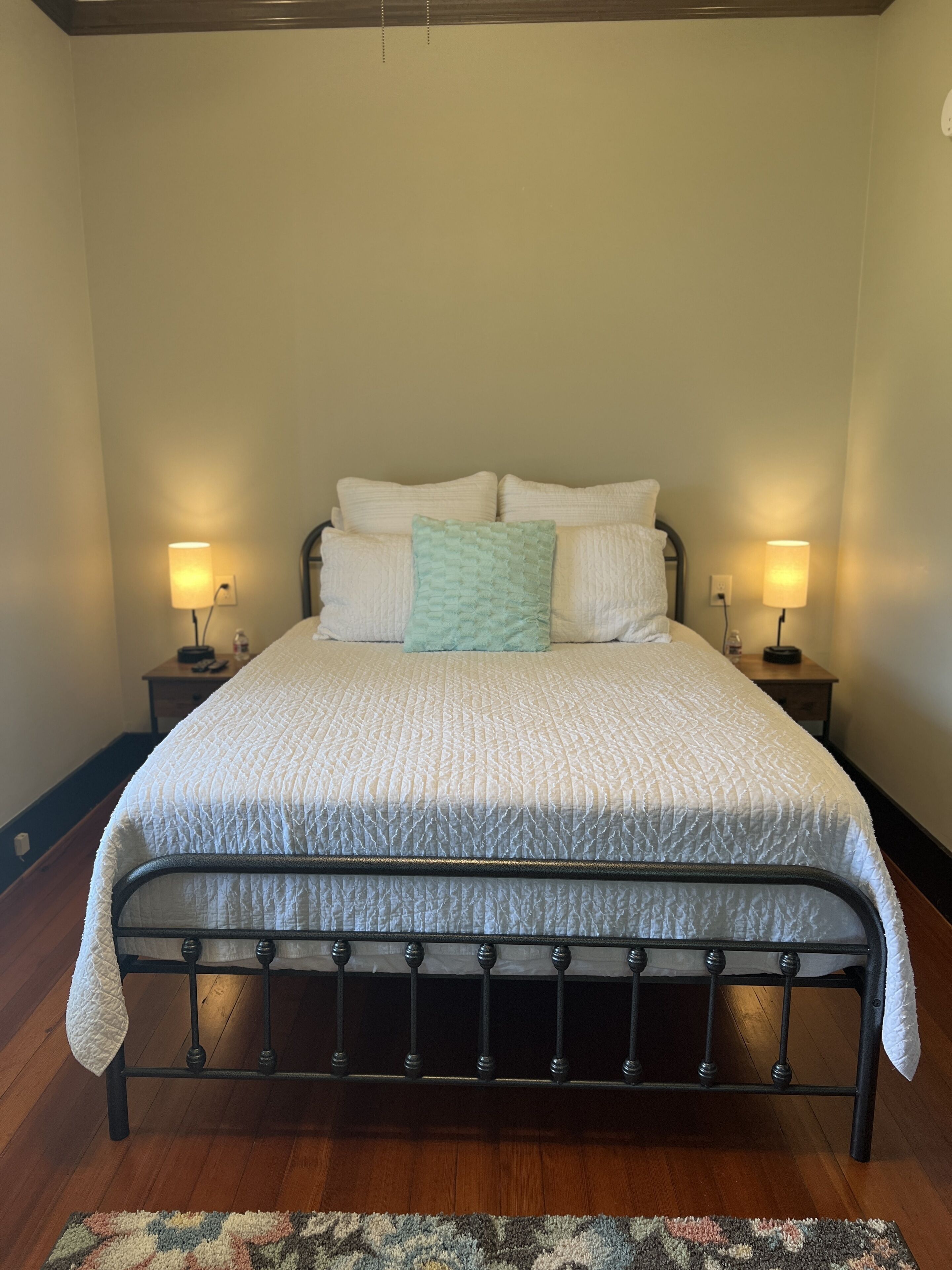 A neatly made bed with a quilted cover, two bedside lamps, and a wooden floor.
