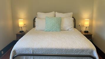 A neatly made bed with a quilted cover, two bedside lamps, and a wooden floor.