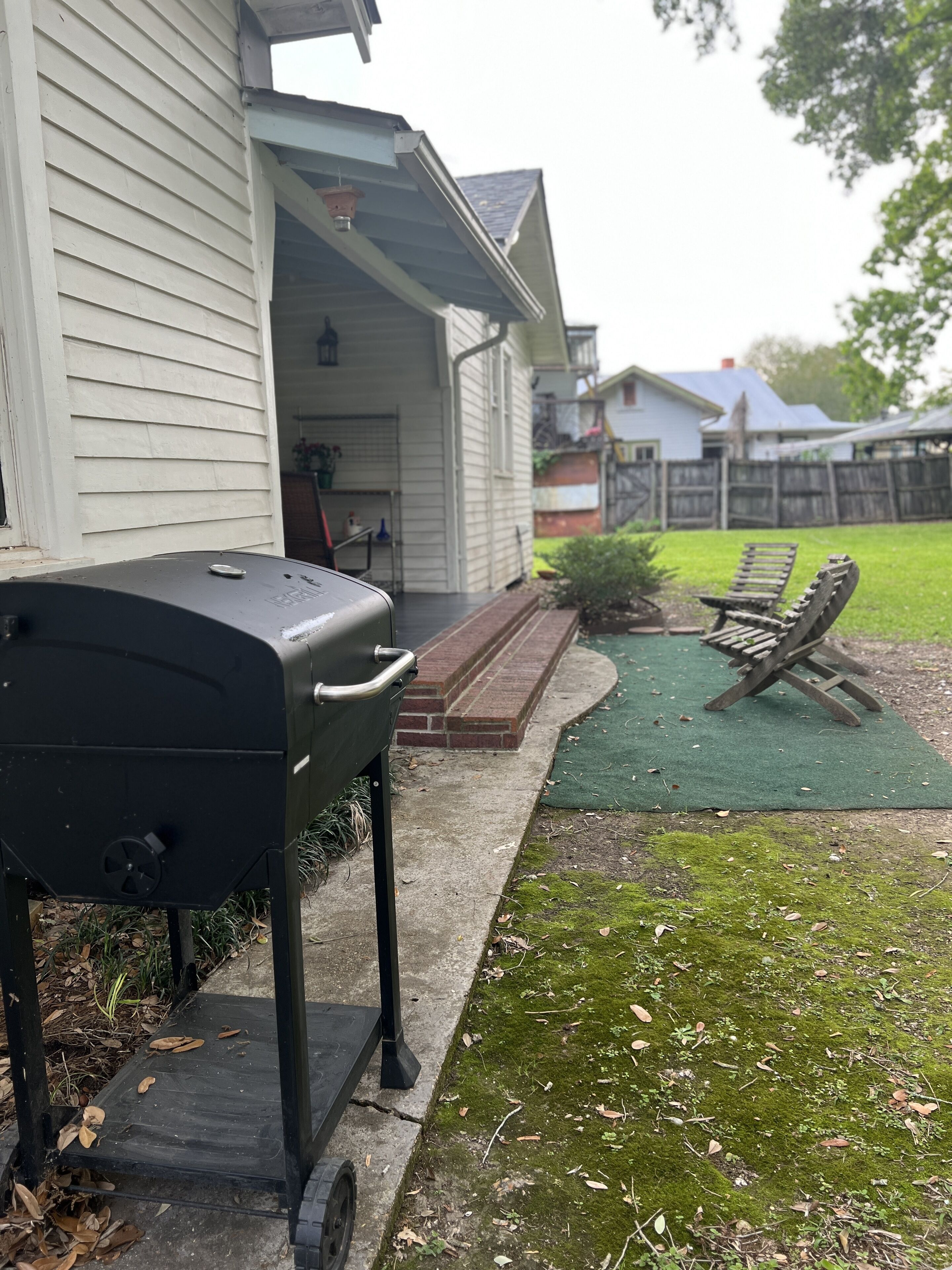 A barbecue grill outside a house with a brick pathway leading to a green lawn area.