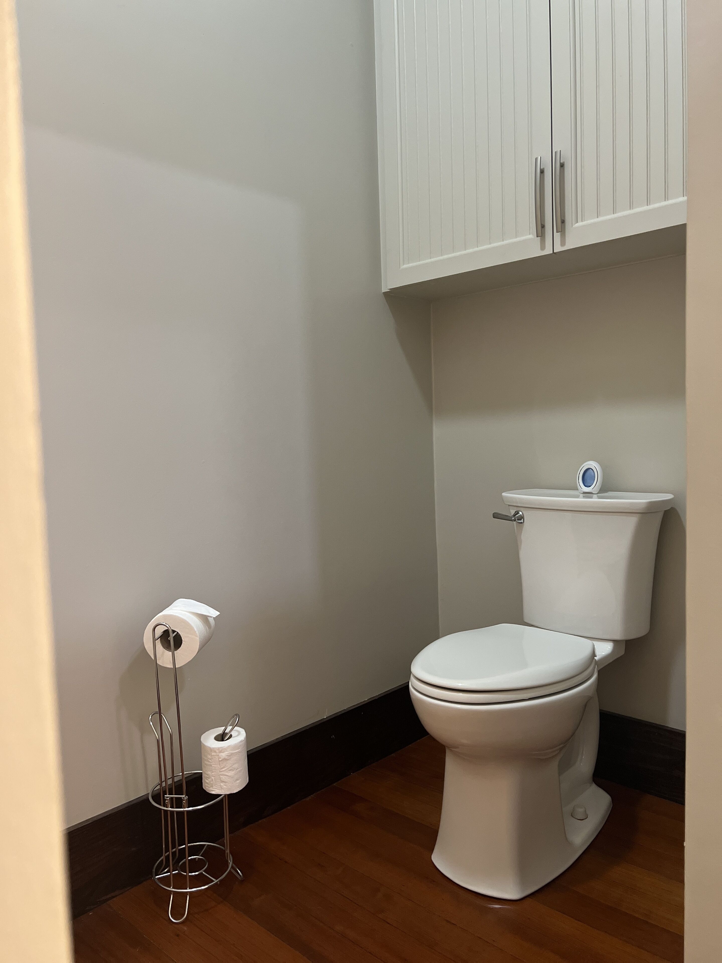 Une salle de bain comprenant des toilettes, un porte-rouleau de papier toilette et un meuble au-dessus des toilettes.