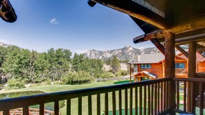 A wooden deck with a view of a mountain landscape, a wooden house, and a small pond. - Black Canyon Inn Unit A4/5 (Estes Park)