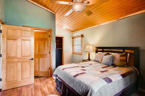 Une chambre avec un plafond en bois, un lit recouvert d’une courtepointe, une table de chevet et une porte.