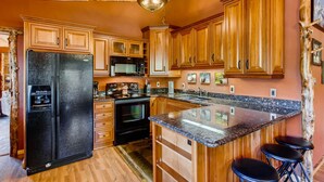 A kitchen with wooden cabinets, a black refrigerator, a microwave, and a granite countertop. - Black Canyon Inn Unit A4/5 (Estes Park)