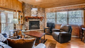 A cozy living room with a stone fireplace, wooden walls, and large windows. - Black Canyon Inn Unit A4/5 (Estes Park)