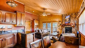A cozy cabin interior with wooden floors, a stone fireplace, a dining area, and a kitchen with wooden cabinets and a dishwasher. - Black Canyon Inn Unit A4/5 (Estes Park)