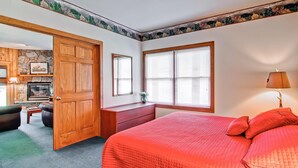 Een slaapkamer met een groot bed, een houten deur, een dressoir, een raam met luiken en een open haard met een stenen muur.