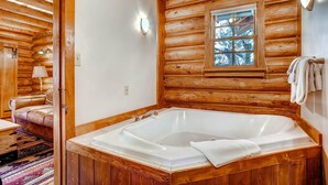 A log cabin interior with a large wooden bathtub, a window with a view, and a cozy seating area.