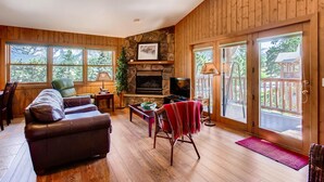 A cozy living room with a stone fireplace, leather sofa, and large windows offering a view of the outdoors.