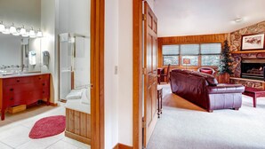 A bathroom with a red vanity, a mirror, and a shower. The living room has a leather sofa, a fireplace, and a stone wall.