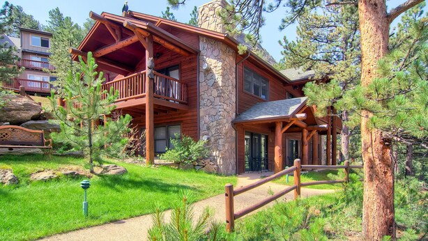 A log cabin-style building with a stone chimney, a balcony, and a stone wall.