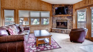 Ein gemütliches Wohnzimmer mit Kamin aus Stein, Holzwänden, einer Ledersofa und einem Fernseher, der über dem Kamin angebracht ist.