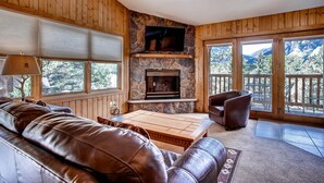 Ein gemütliches Wohnzimmer mit Kamin aus Stein, einer Ledersofa und großen Fenstern mit Blick auf die Berge.