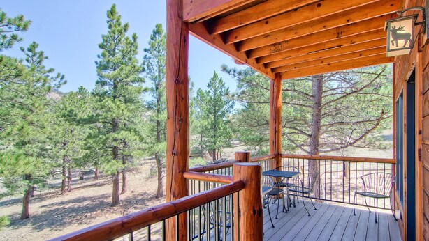 A wooden deck with a railing, a table with chairs, and a deer sign. - Black Canyon Inn Unit F3 (Estes Park)