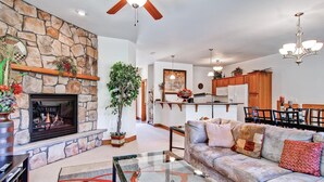 A spacious living room with a stone fireplace, a sofa, and a dining area with wooden cabinets. - Black Canyon Inn Unit F3 (Estes Park)