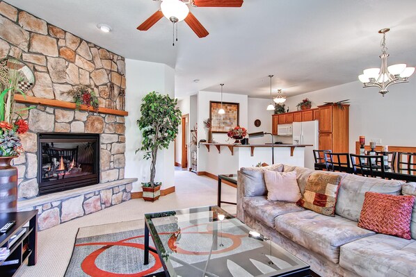 A spacious living room with a stone fireplace, a sofa, and a dining area with wooden cabinets. - Black Canyon Inn Unit F3 (Estes Park)