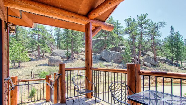 A wooden deck with metal chairs and a table, overlooking a rocky landscape with pine trees. - Black Canyon Inn Unit F10 (Estes Park)