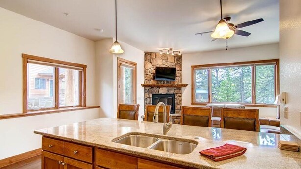 A kitchen with a stone fireplace, wooden cabinets, a large island with a sink, and two pendant lights. - Black Canyon Inn Unit H1 Deluxe (Estes Park)