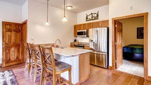 A kitchen with wooden cabinets, a central island with bar stools, stainless steel appliances, and pendant lighting. - Black Canyon Inn Unit H1 Deluxe (Estes Park)