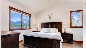 Un dormitorio con una cama grande, dos mesitas de noche, un cabecero de madera y vistas a la montaña a través de un amplio ventanal.