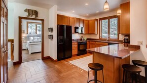 Una cocina moderna con armarios de madera, un refrigerador negro, una estufa y una isla grande con taburetes de bar.