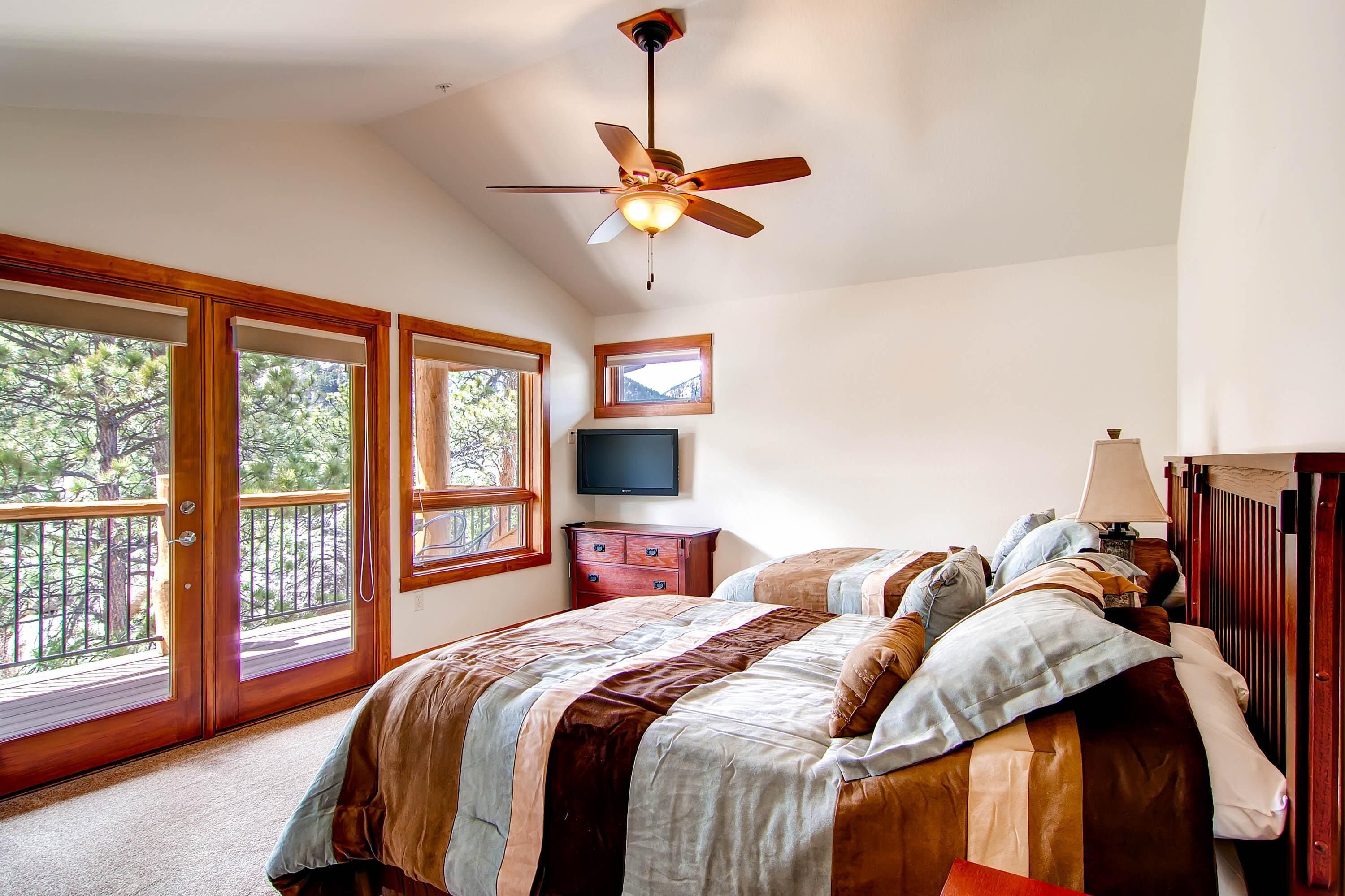 A bedroom with a bed, a ceiling fan, a dresser, a TV, and a window with a view of trees.