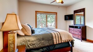 A bedroom with a bed, a ceiling fan, a dresser, a TV, and a window with a view of trees. - Black Canyon Inn Unit H4 Deluxe (Estes Park)