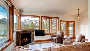A living room with a stone fireplace, leather sofa, and large windows overlooking mountains. - Black Canyon Inn Unit H4 Deluxe (Estes Park)