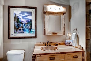 A bathroom with a rustic wooden vanity, a framed wildlife painting, and a vintage-style mirror. - Black Canyon Inn Unit A6 Deluxe (Estes Park)