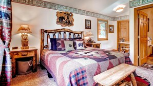 Quarto aconchegante com cama de madeira, colcha, mesa pequena e mesa de cabeceira com abajur.