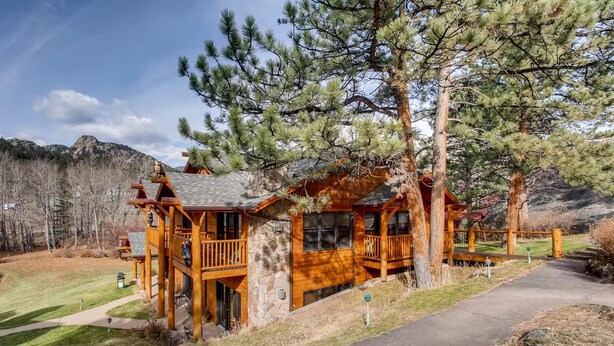 Une cabane en bois, construite sur des fondations en pierre, entourée d’arbres et avec une chaîne de montagnes en toile de fond.