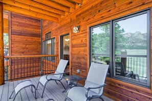 A wooden deck with two chairs and a table, large windows with a view of trees and a lake, and a wooden railing. - Black Canyon Inn Unit F7 Deluxe (Estes Park)