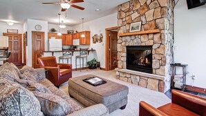 A living room with a stone fireplace, a ceiling fan, and a kitchen in the background. - Black Canyon Inn Unit F7 Deluxe (Estes Park)