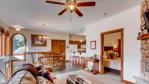 A spacious living room with a ceiling fan, a dining area with wooden furniture, a kitchen with a stone fireplace, and a bedroom with a bed and a nightstand. - Black Canyon Inn Unit F4 (Estes Park)